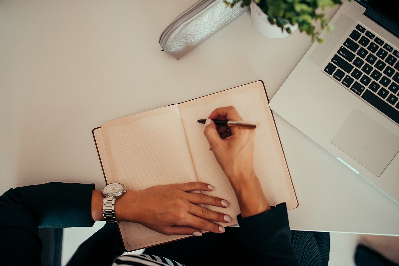 内容站站长在书桌前一边看笔记本电脑一边记录，示意展示广告变现的日常运营